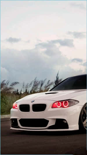 白色BMW跑車帶紅色頭燈，停泊在陰天下草旁的道路上。