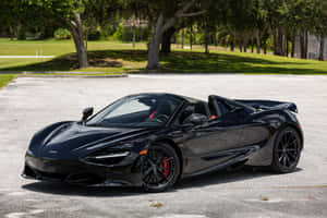 黑色McLaren 720S Spider開篷車停在陽光明媚的戶外停車場，周圍有綠樹。