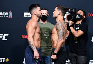 兩名赤裸上身的MMA拳手在UFC稱重儀式上互相凝視，周圍有相機。