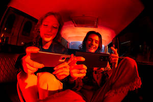 兩個人在夜間的車內被紅色手機光照亮而大笑。