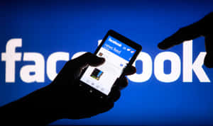 手部拿著手機，顯示Facebook新聞動態，背景是藍色標誌。
