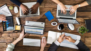 Team of professionals working together on digital devices at a wooden desk.