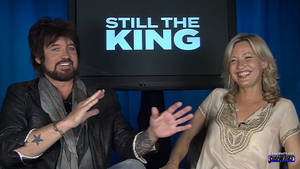 兩位微笑的主持人在電視採訪中做手勢，屏幕上顯示「STILL THE KING」。