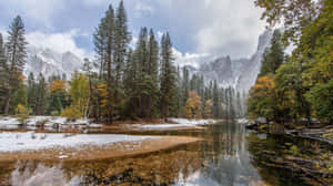 白雪覆蓋河岸和樹木，平靜的溪流映照出秋天的色彩和遠方的山峰。
