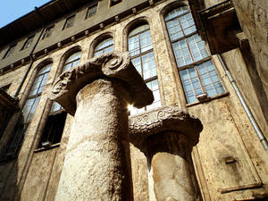 帶有雕刻柱頭的風化石柱，位於一座擁有拱形窗戶的歷史建築前。