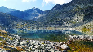 平靜的山湖，四周環繞著岩石地形和巍峨的山峰，天空湛藍。