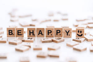木製字母磚在白色背景上拼出 'BE HAPPY'，並有一個笑臉磚。 — 開心 GIF 壁紙