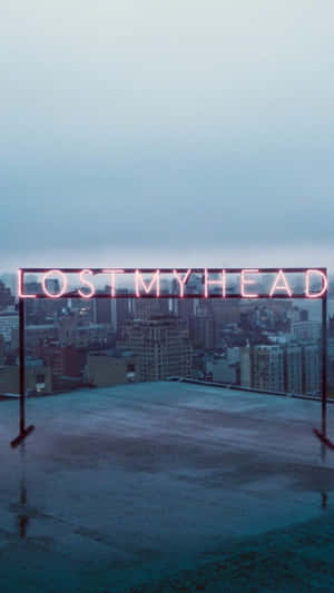 寫著 lost my head 的霓虹燈牌，位於濕漉漉的屋頂上，俯瞰黃昏時分的城市。 — 高對比 壁紙