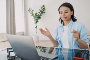身穿藍色恤衫的女性在家庭辦公室用筆記本電腦和植物進行視像通話。 — 放大 壁紙