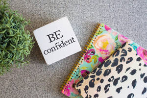 一個勵志方塊，上面寫著「BE confident」，旁邊有圖案筆記本和一棵綠色植物。