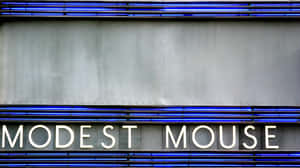灰色牆上帶有藍色燈光和白色字樣的 Modest Mouse 霓虹招牌。