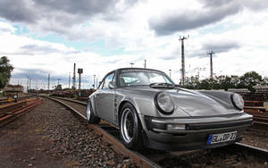 銀色經典保時捷911停泊在火車軌道上，背景為多雲天空。