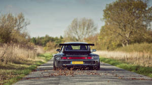 黑色保時捷911 Turbo在鄉村道路上行駛，散落秋天的落葉。