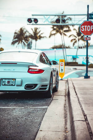 銀色保時捷 Turbo S 停在行人過路處，後面有棕櫚樹和海洋。
