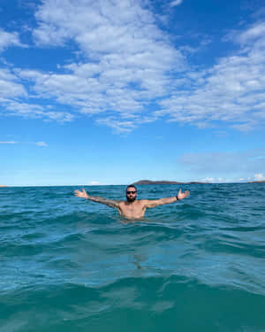 有紋身和太陽眼鏡的男人在藍天下於海水中張開雙臂