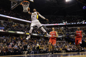 籃球運動員在空中越過防守者灌籃，場館擠滿人。