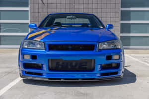 帶有賽車條紋的藍色日產Skyline R34停在一棟現代建築前。