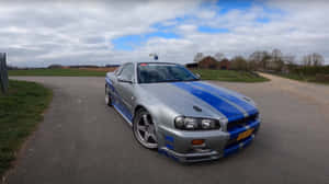 銀色日產Skyline R34，帶有藍色賽車條紋，停在鄉村道路上。