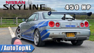 銀色日產Skyline跑車帶藍色條紋，停泊在木柵欄附近的碎石上。