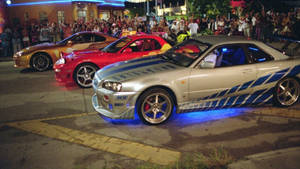 三輛定制街頭賽車在夜間停泊，帶有藍色車底燈光，人群觀看。