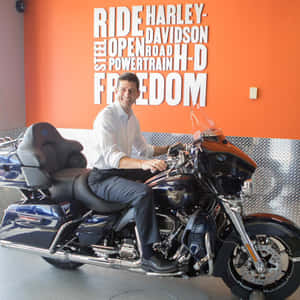 男子微笑著坐在黑色Harley-Davidson電單車上，身處有橙色牆壁文字的陳列室。