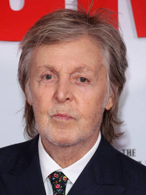Paul McCartney 喺活動中着西裝同花卉圖案領呔，背景係紅色同白色。 — 肖像 壁紙