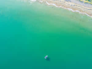 一艘小船獨自漂浮在沙灘附近清澈的碧綠海水中。 — 海浪 壁紙