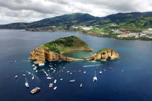 島嶼擁有自然岩石拱門和碧綠水池，周圍船隻在藍色海洋中。 — MacBook Pro M4 壁紙