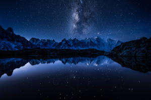 星空下積雪的山巒，夜晚倒映在平靜的湖面。