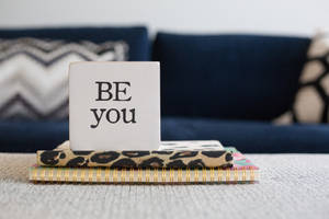 白色方塊上寫著「BE you」，放在筆記本上，靠近海軍藍沙發。