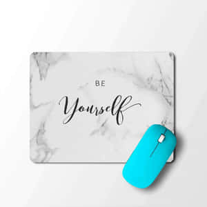 白色大理石滑鼠墊，帶有 'Be Yourself' 文字和一個青色滑鼠，置於白色表面上。