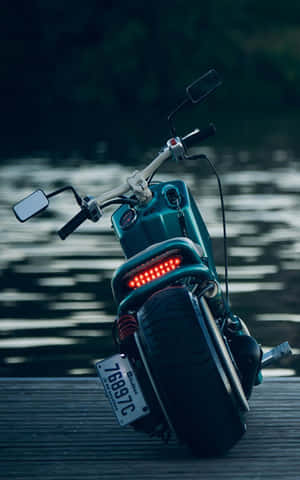青綠色電動滑板車，帶紅色燈光，黃昏時停放在水邊木製碼頭上。