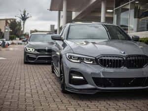 兩輛灰色BMW汽車停泊在現代建築附近的磚砌車道上。