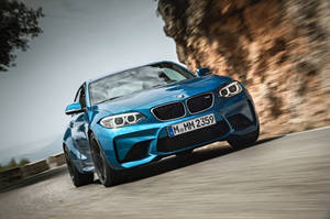 藍色BMW M2 Coupe在山路上疾馳，帶有模糊動態效果。