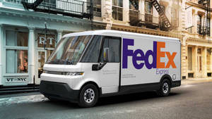 白色FedEx電動送貨車停泊在歷史建築附近的城市街道上。