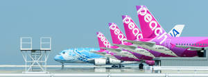 四架色彩繽紛的桃子航空飛機停放在潮濕機場停機坪上，帶有金屬樓梯。