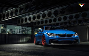 藍色BMW M4配紅色輪圈，夜間停在橋下，背後是城市燈光。