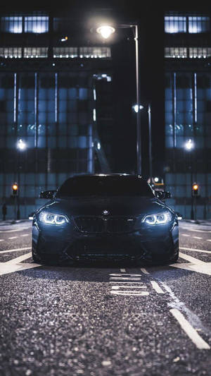 黑色BMW跑車在夜間停放在濕漉漉的城市街道上，在街燈下。