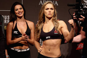 UFC拳手在稱重活動中自信地擺姿勢，旁邊有一位微笑的女性。