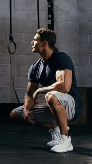 運動型男人在健身房裡蹲下，背景是磚牆和體操吊環。 — 健身房 壁紙