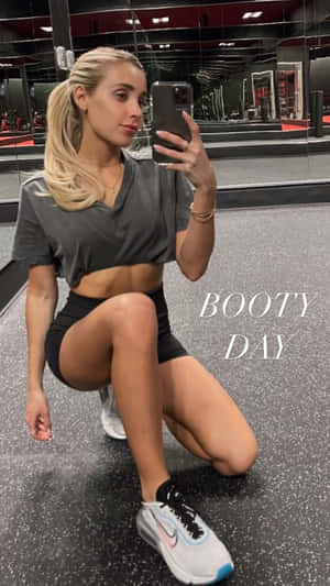穿著健身服裝的女性對著鏡子自拍，帶有「BOOTY DAY」文字。 — 健身 壁紙