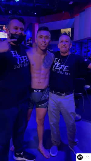 三名男子在藍色燈光下於UFC活動後台擺姿勢。