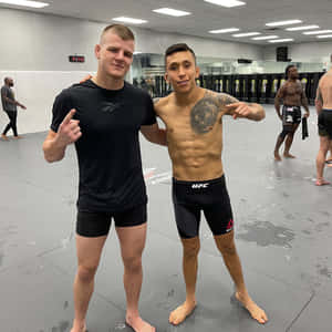 兩名男性拳手在UFC訓練設施中擺姿勢，背景有沙包。