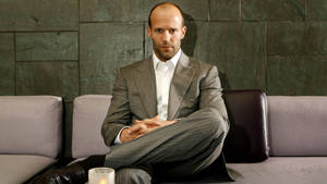 Jason Statham 身穿灰色西裝，盤腿坐在沙發上，旁邊點著蠟燭。
