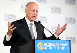 穿西裝的男子在 Global Climate Action Summit 講台上發言，雙手做手勢。 — 政治 壁紙