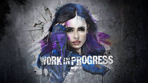 一位紫髮女性，在裂紋混凝土牆上有油漆飛濺，並帶有「WORK IN PROGRESS」文字。