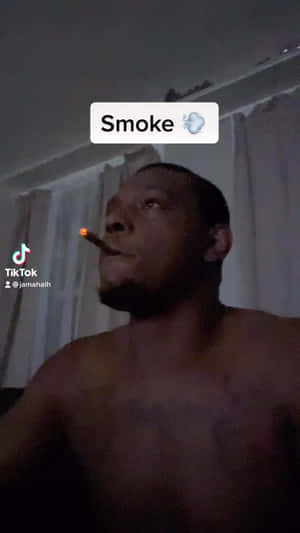 一名赤裸上身的男子在夜間於室內抽著點燃的雪茄煙。