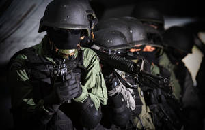 一排身穿戰術裝備的武裝士兵站在昏暗的光線中。