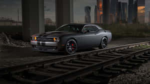 灰色Dodge Challenger停喺廢棄火車軌上，背景係黃昏城市天際線。