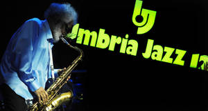 色士風手在夜間於發光的綠色Umbria Jazz標誌下表演。 — 猶他爵士 壁紙